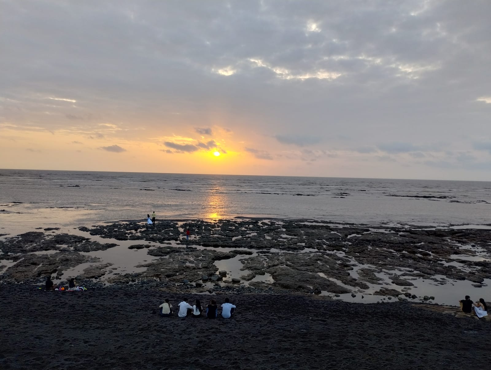 Devka Beach, Daman. Black sand, rock pools, and the sun going into the sea.